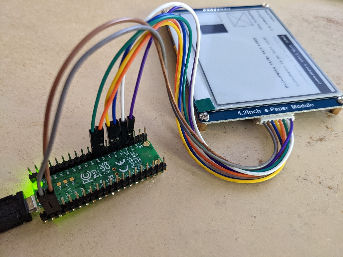 Picture showing PiPicoW upside down with coloured wiring going from pins listed in table to a 4.2 Inch e-Paper module, itself showing the results of the WaveShare demo Python script onscreen